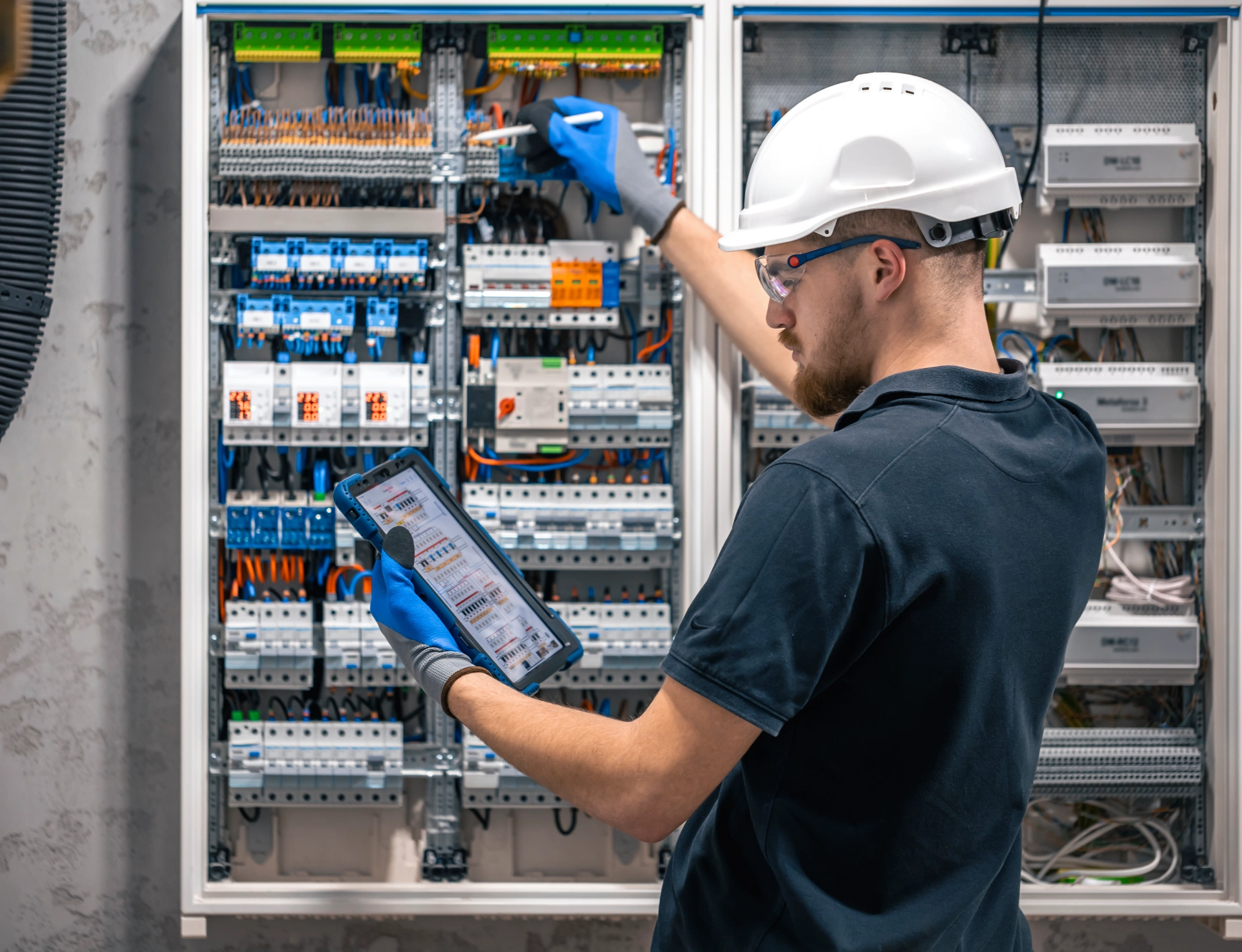electrical technician working switchboard with fuses uses tablet